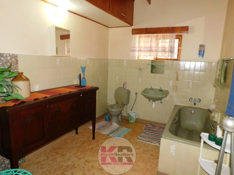 A dated bathroom featuring a bathtub, wall-mounted basin, toilet, and built-in cabinetry with tiled wall finishes.