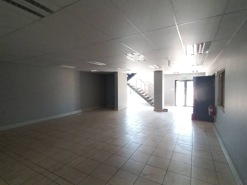 Spacious open-plan industrial office or showroom area featuring tiled flooring, suspended ceilings with recessed lighting, and a staircase leading to an upper level.