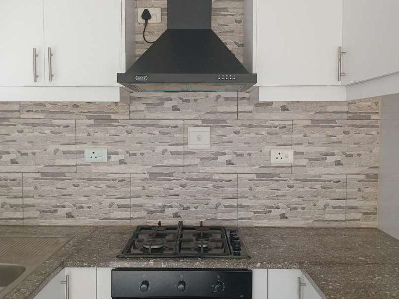 A modern kitchen featuring white cabinetry, stone-look backsplash, built-in oven, gas hob, and extractor fan.