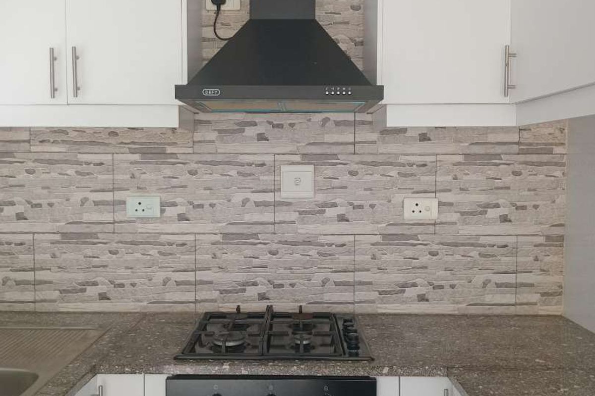A modern kitchen featuring white cabinetry, stone-look backsplash, built-in oven, gas hob, and extractor fan.