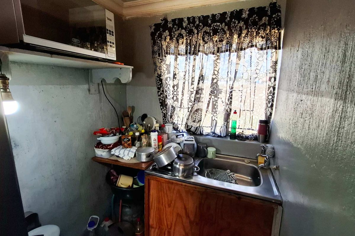 A compact kitchen area featuring a stainless steel sink, wooden base cabinetry, and a built-in microwave shelf, requiring cosmetic updates and maintenance.