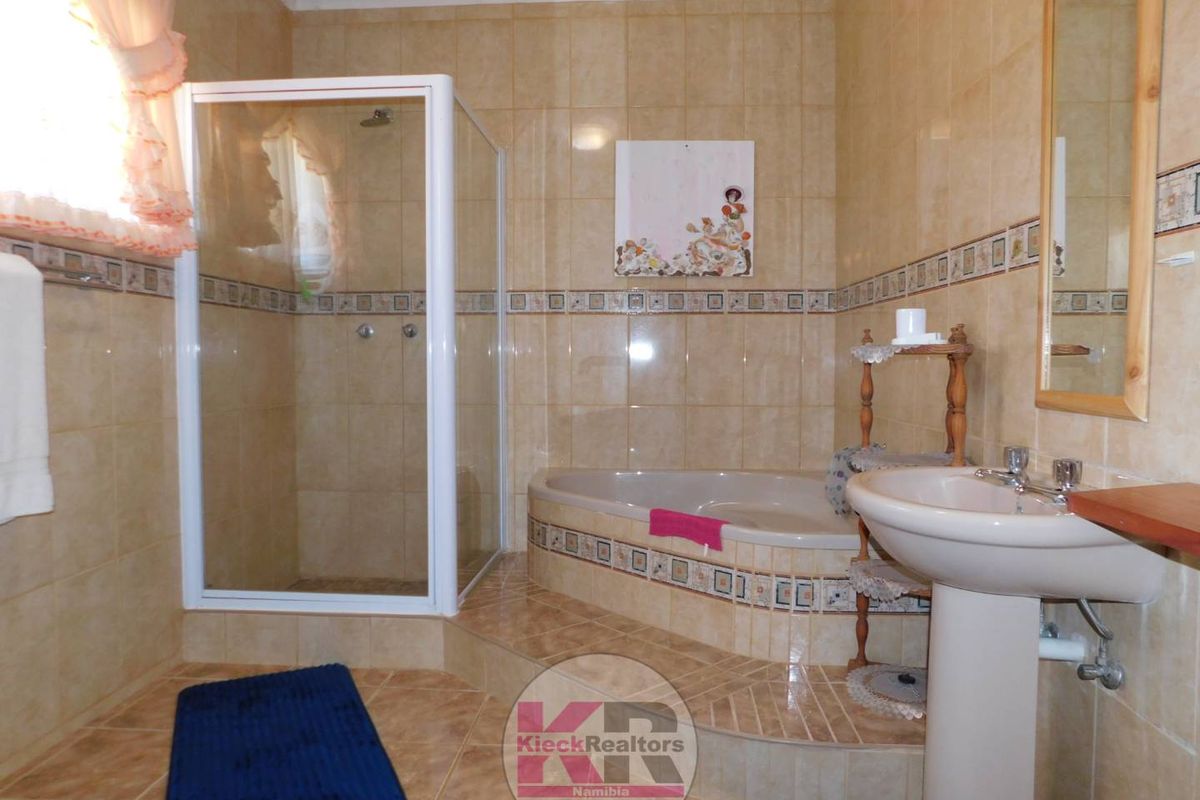 A functional bathroom featuring a tiled shower enclosure, a built-in bathtub on a raised platform, and a pedestal sink with neutral wall tiling.