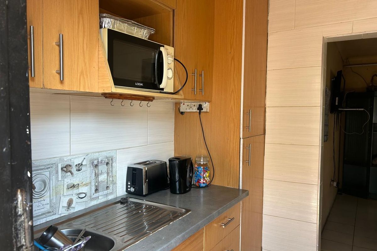A functional kitchen area featuring wood-look cabinetry, a stainless steel sink, and tiled splashback, providing essential storage and preparation space.