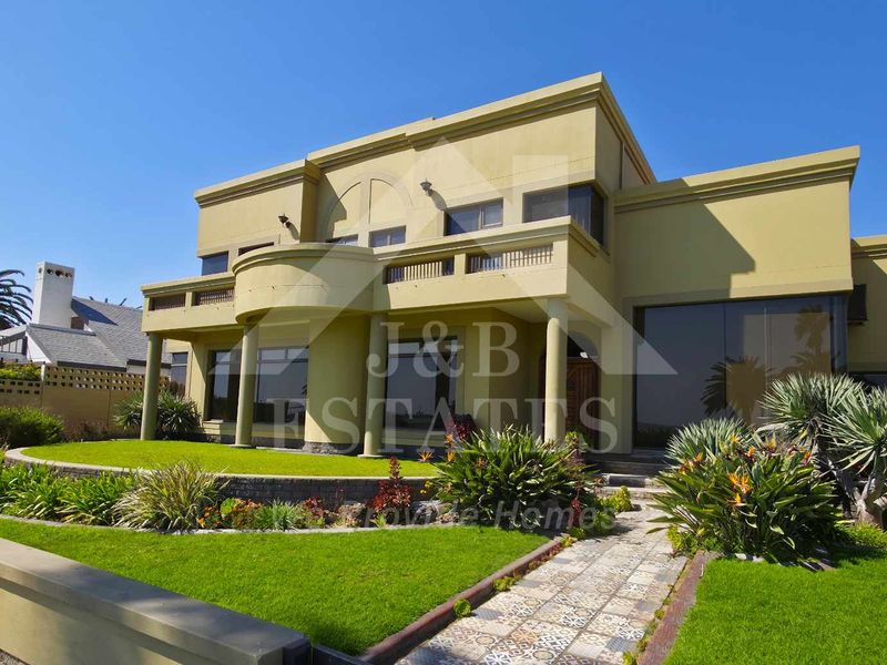 A well-maintained two-story residential property featuring a curved balcony, decorative columns, and a landscaped front garden with a paved walkway.