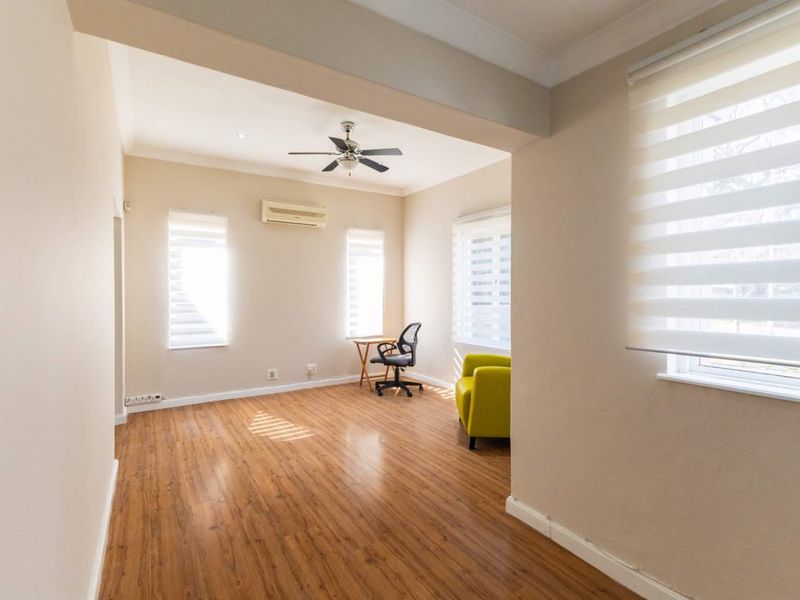 A bright and spacious living area featuring laminate flooring, a ceiling fan, and a wall-mounted air conditioning unit with neutral wall finishes.