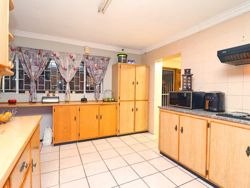 A functional kitchen featuring wooden cabinetry, tiled flooring, and a tiled backsplash, offering a practical layout with ample storage space.