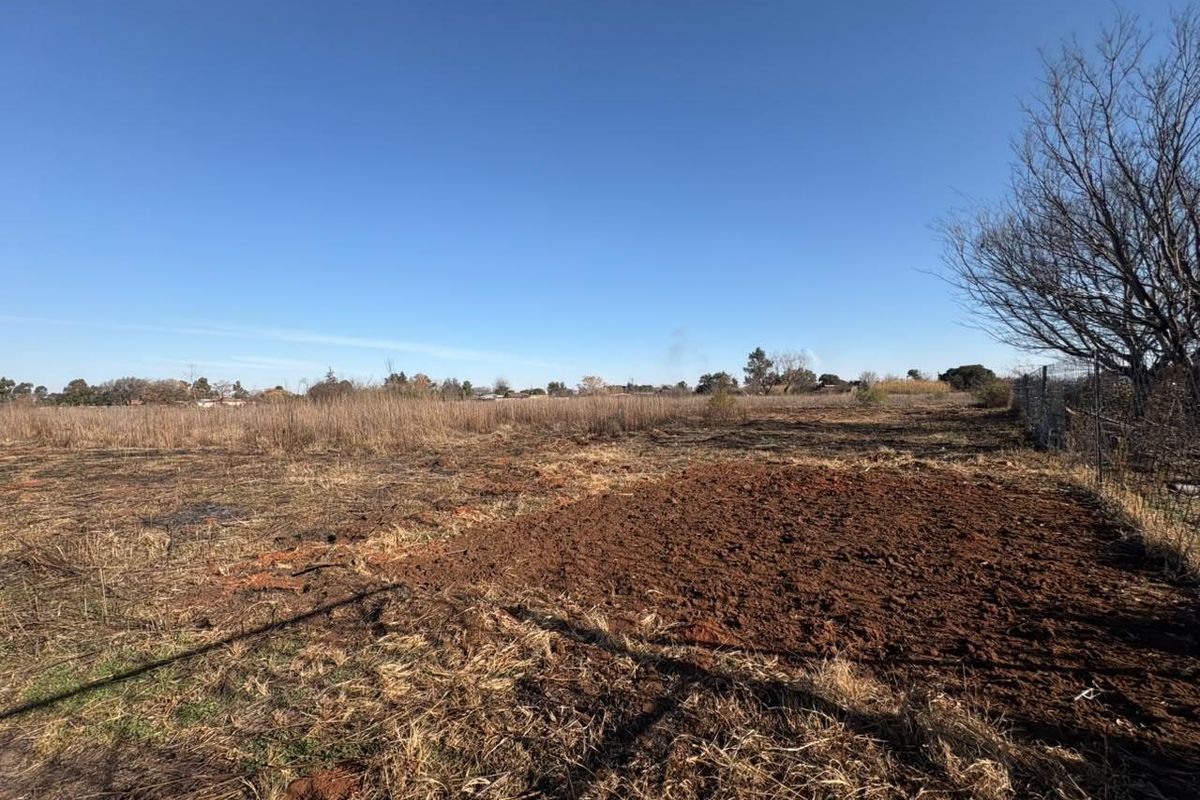 A view of a vacant residential plot featuring cleared soil and perimeter wire fencing under a clear blue sky.