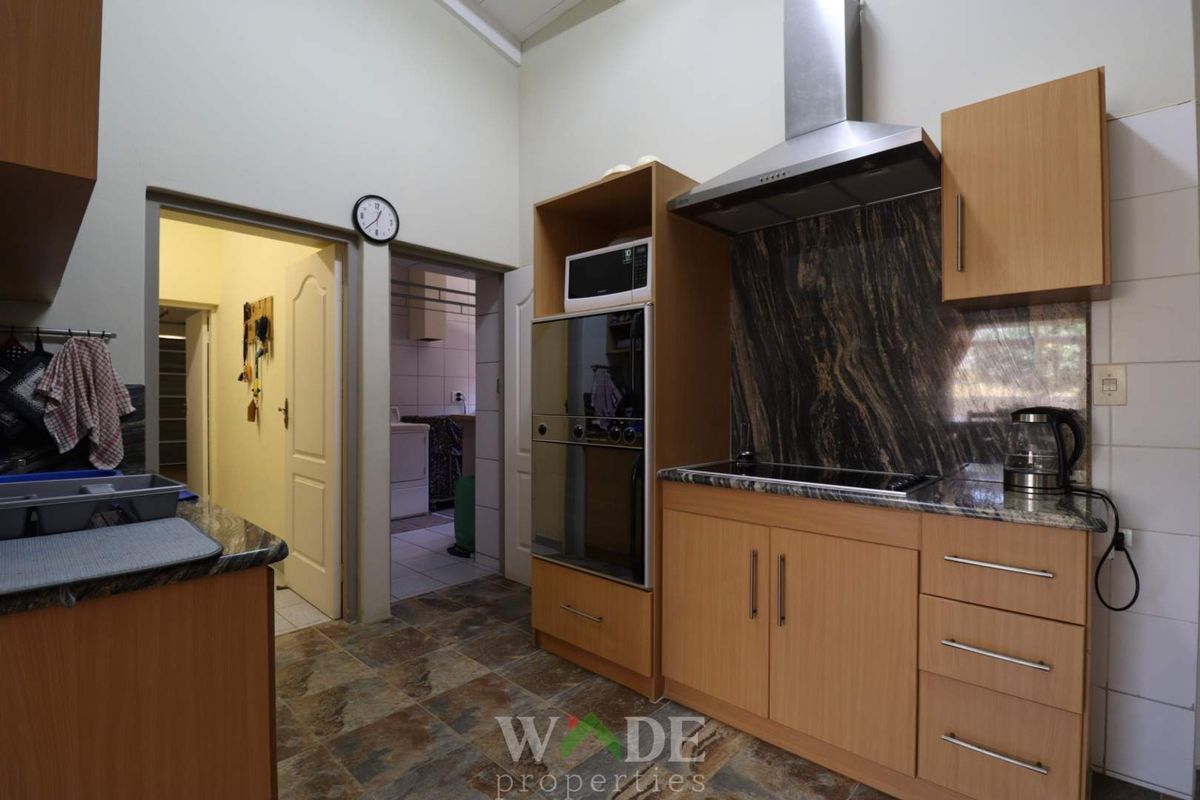 A functional kitchen featuring wood-finish cabinetry, granite countertops, a built-in oven, and a stainless steel extractor fan, with an adjacent scullery area.