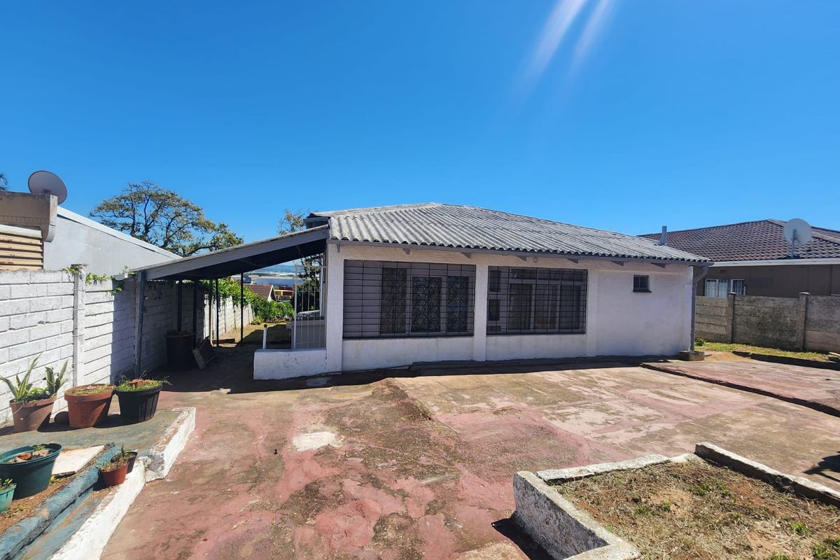 Rear exterior view of the house featuring a concrete patio area, security bars on windows, and a corrugated roof structure.