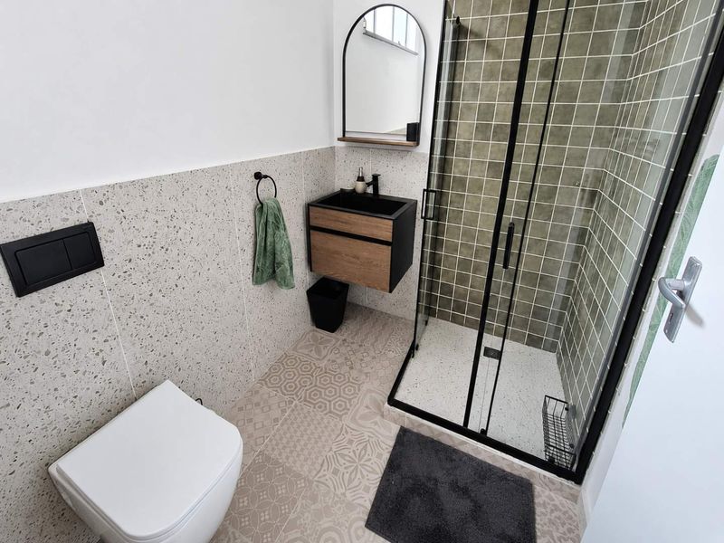 Modern bathroom featuring a wall-hung toilet, vanity basin, and a walk-in shower with black frame and stylish patterned floor tiles.