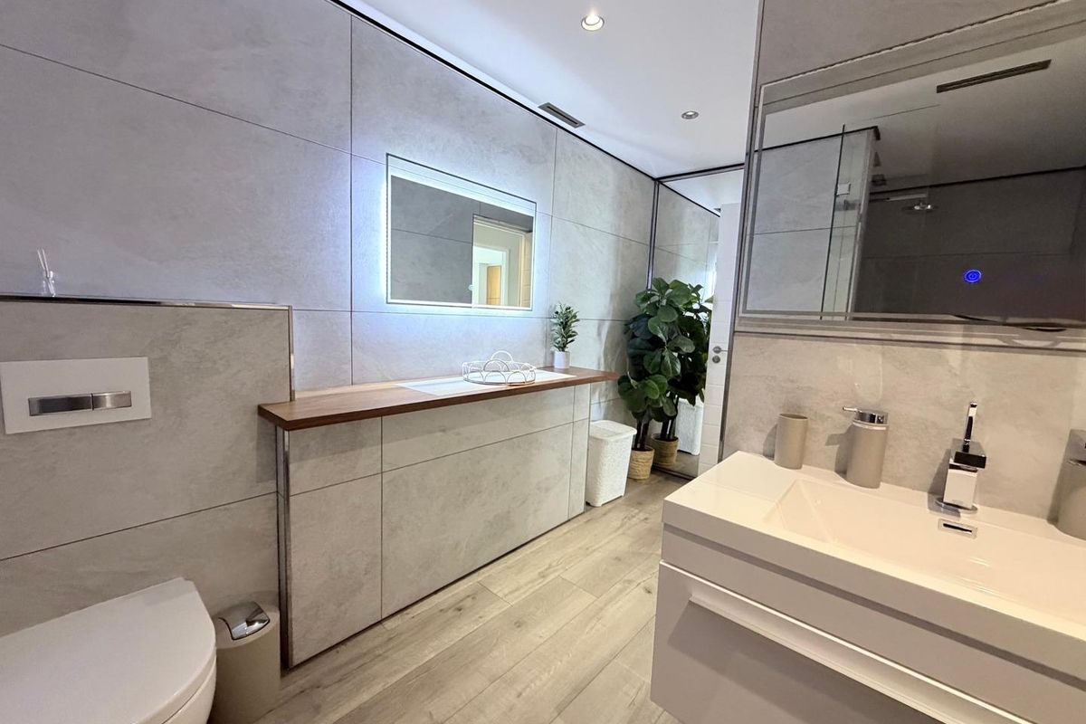 Modern, well-appointed bathroom featuring large format wall tiles, a sleek integrated vanity, wall-mounted toilet, and contemporary backlit mirror with recessed lighting.