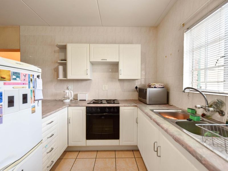 A functional kitchen featuring white cabinetry, laminate countertops, a built-in electric oven and hob, and a double bowl stainless steel sink with tiled finishes.