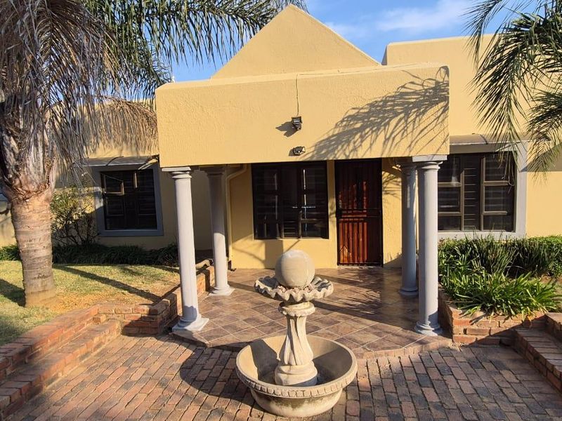 Front entrance of the house featuring a covered tiled porch with decorative columns, a brick paved walkway, and a central stone water feature.