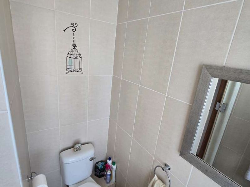 A compact bathroom featuring neutral wall and floor tiling, a standard toilet, and a wall-mounted mirror.