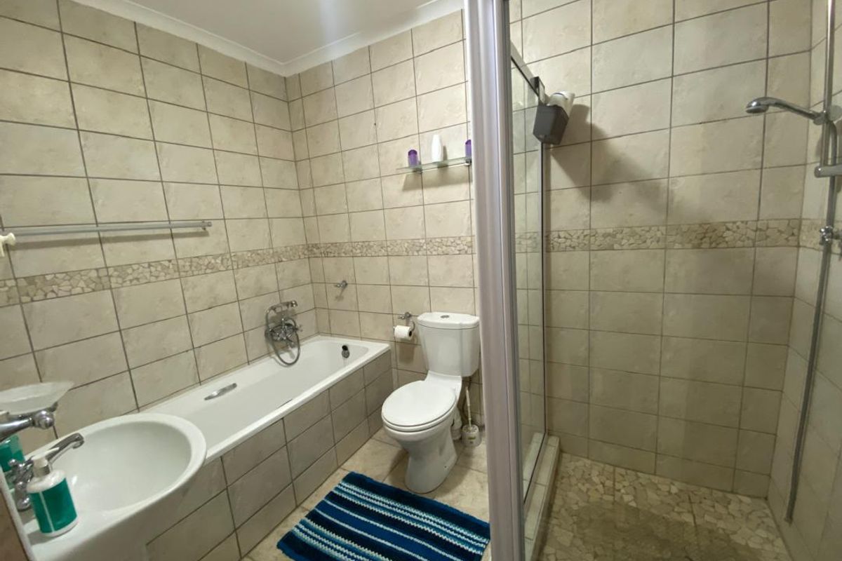 A functional bathroom featuring a pedestal basin, a bathtub with handheld shower mixer, and a separate glass-enclosed shower cubicle with tiled walls.