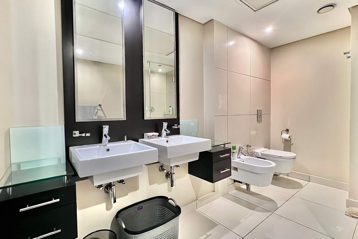 Modern bathroom featuring a double wall-mounted vanity, wall-hung toilet and bidet, large mirrors, and neutral floor-to-ceiling tiling.