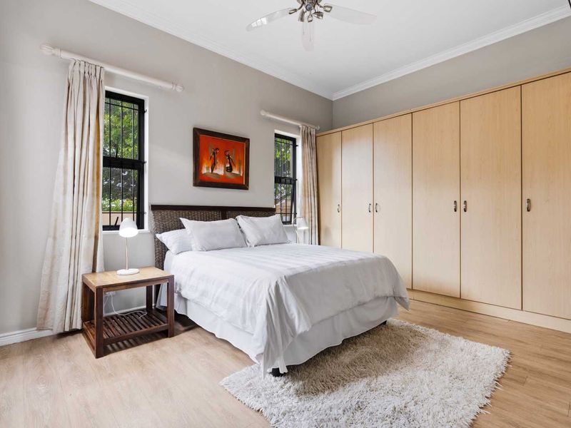 A well-maintained bedroom featuring light wood-look laminate flooring, extensive built-in cabinetry, and a ceiling fan, offering a clean and functional living space.