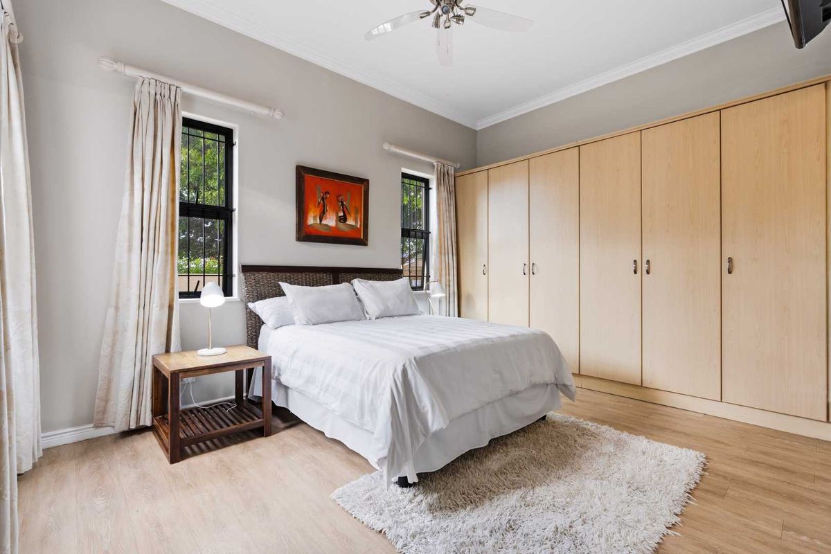 A well-maintained bedroom featuring light wood-look laminate flooring, extensive built-in cabinetry, and a ceiling fan, offering a clean and functional living space.