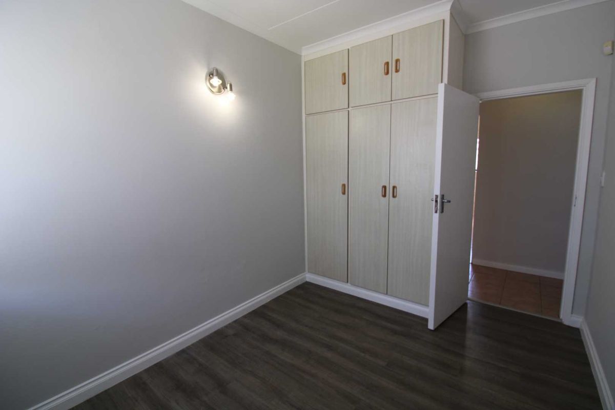 A clean, empty bedroom featuring built-in cupboards with overhead storage, modern laminate flooring, and a wall-mounted light fixture.