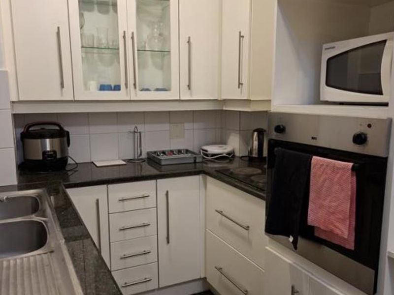 A functional kitchen featuring white cabinetry, granite countertops, a built-in oven, and a stainless steel double sink with tiled flooring.