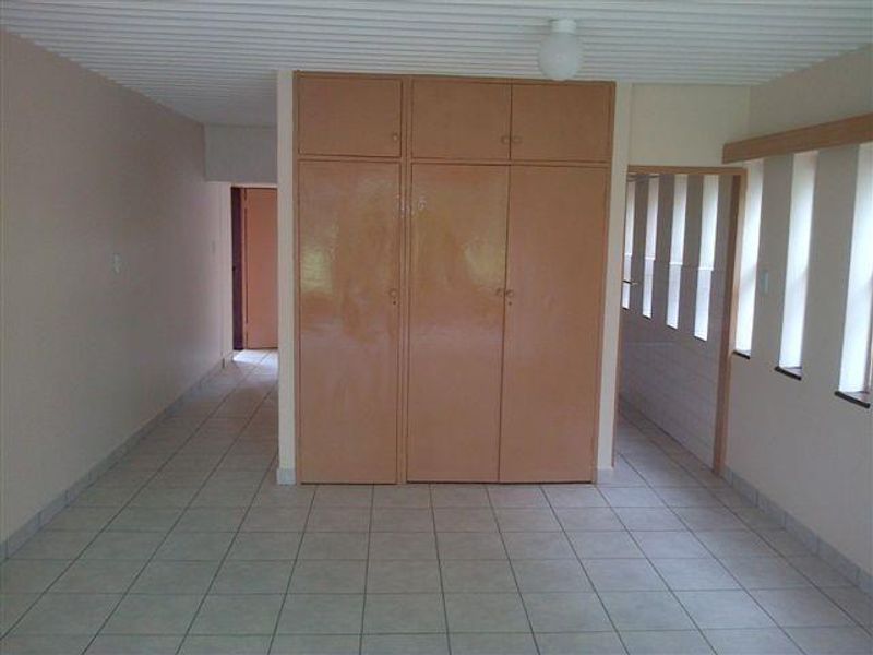 An empty bedroom featuring tiled flooring, a ribbed ceiling, and built-in cupboards, offering a blank canvas for renovation and modernization.