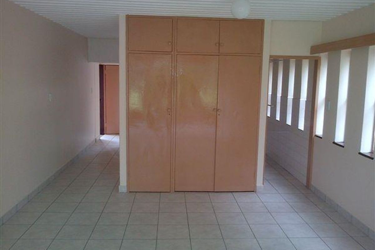 An empty bedroom featuring tiled flooring, a ribbed ceiling, and built-in cupboards, offering a blank canvas for renovation and modernization.