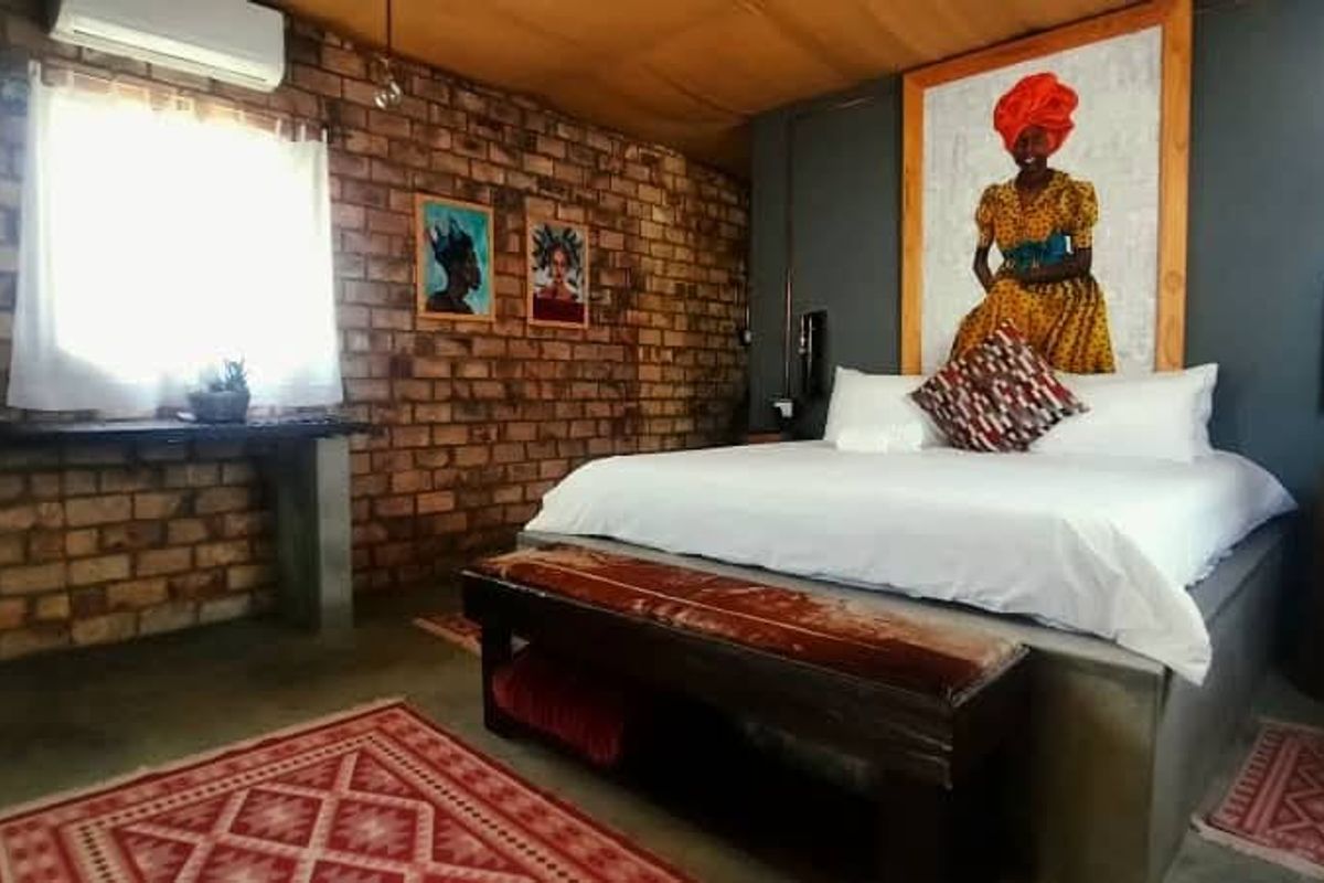 A rustic-style bedroom featuring exposed brick walls, a concrete bed base, and a wall-mounted air conditioning unit.
