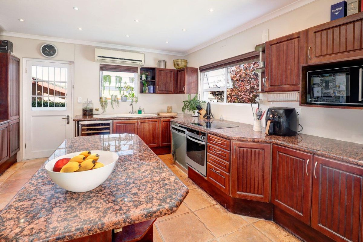 A functional kitchen featuring dark wood cabinetry, granite countertops, a central island, and built-in appliances including an oven and hob.