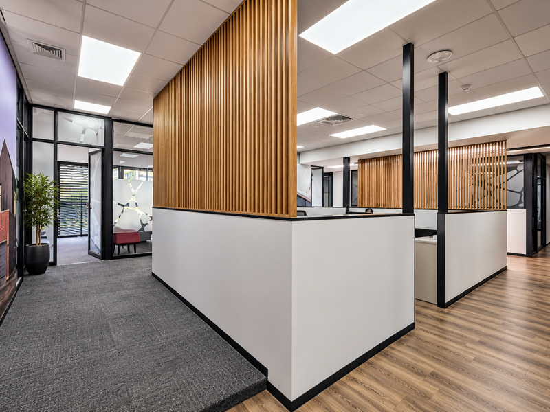 Modern open-plan office space featuring contemporary timber slat partitions, suspended ceilings with recessed lighting, and a mix of carpet and wood-look flooring.