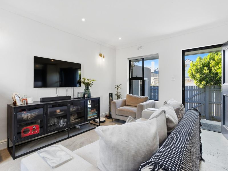 A bright and modern living room featuring recessed downlights, neutral finishes, and direct access to an outdoor area through a sliding glass door.