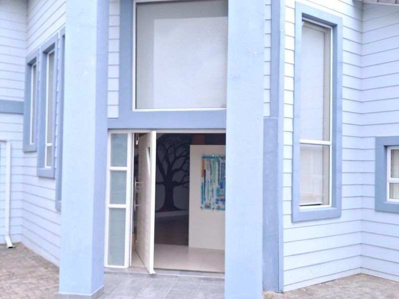 Front elevation of a modern house featuring light blue weatherboard cladding, a prominent double-height entrance, and paved driveway access.