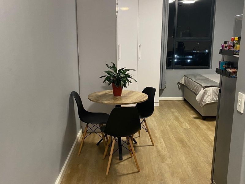 An open-plan studio apartment featuring laminate flooring, a built-in wardrobe, and a large window providing natural light.