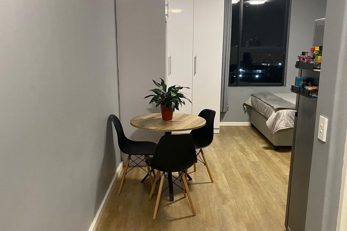 An open-plan studio apartment featuring laminate flooring, a built-in wardrobe, and a large window providing natural light.