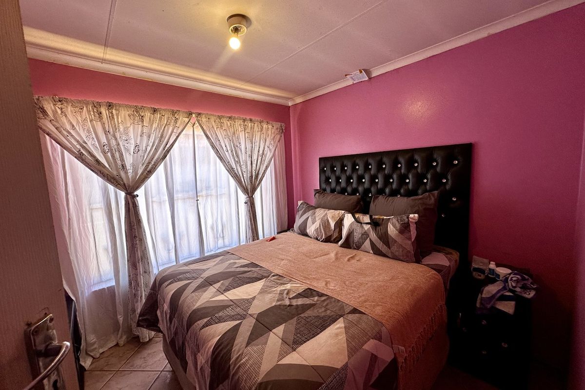 A bedroom featuring tiled flooring and pink painted walls, requiring some maintenance to the ceiling and electrical fixtures.