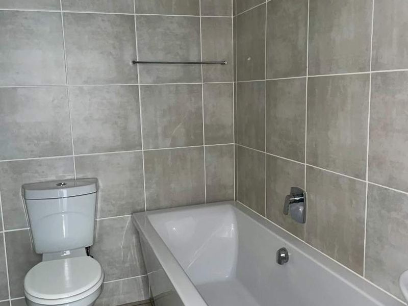 A clean, modern bathroom featuring neutral grey wall and floor tiles, a white bathtub, and a standard toilet.