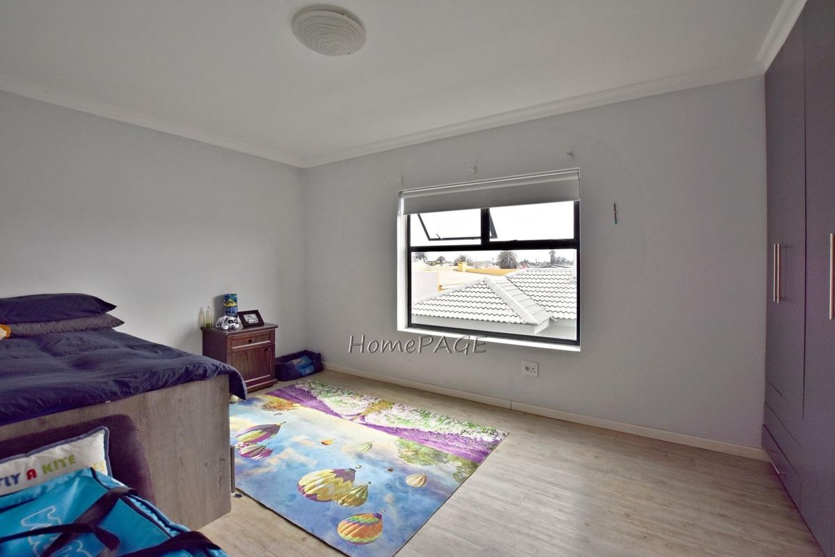 A bedroom featuring light-toned laminate flooring, a built-in wardrobe, and a window with a roller blind.