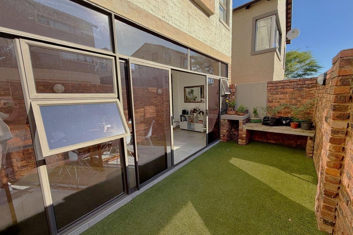 Rear courtyard featuring artificial lawn, built-in brick braai area, and large sliding glass doors providing seamless access to the interior living space.