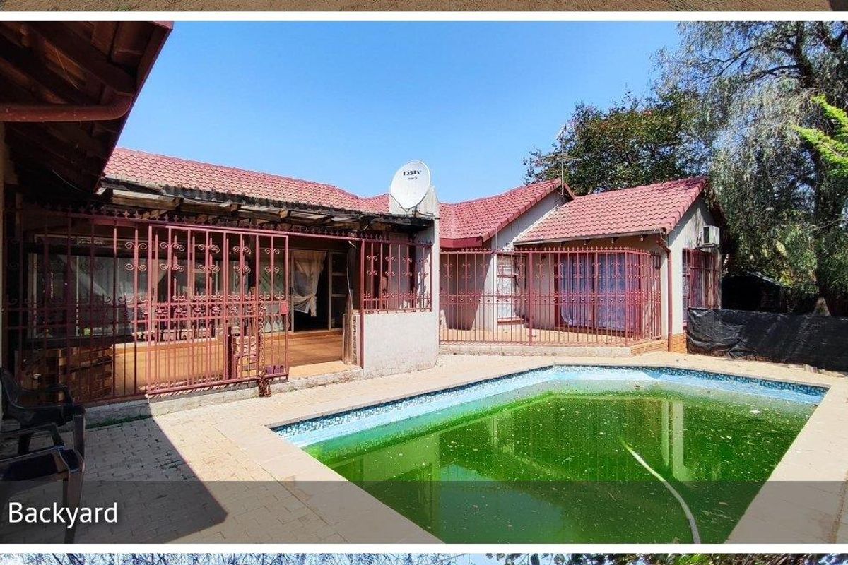 Rear exterior view featuring a swimming pool, paved patio area, and security-gated access to the main house structure.