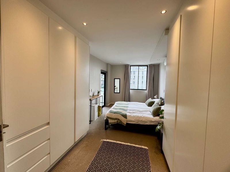 A well-lit bedroom featuring extensive built-in cupboard storage, recessed downlighting, and direct access to an outdoor area via a sliding door.