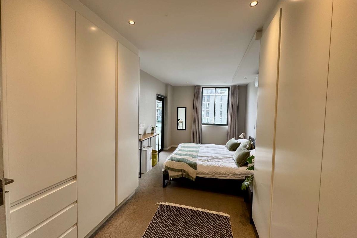 A well-lit bedroom featuring extensive built-in cupboard storage, recessed downlighting, and direct access to an outdoor area via a sliding door.
