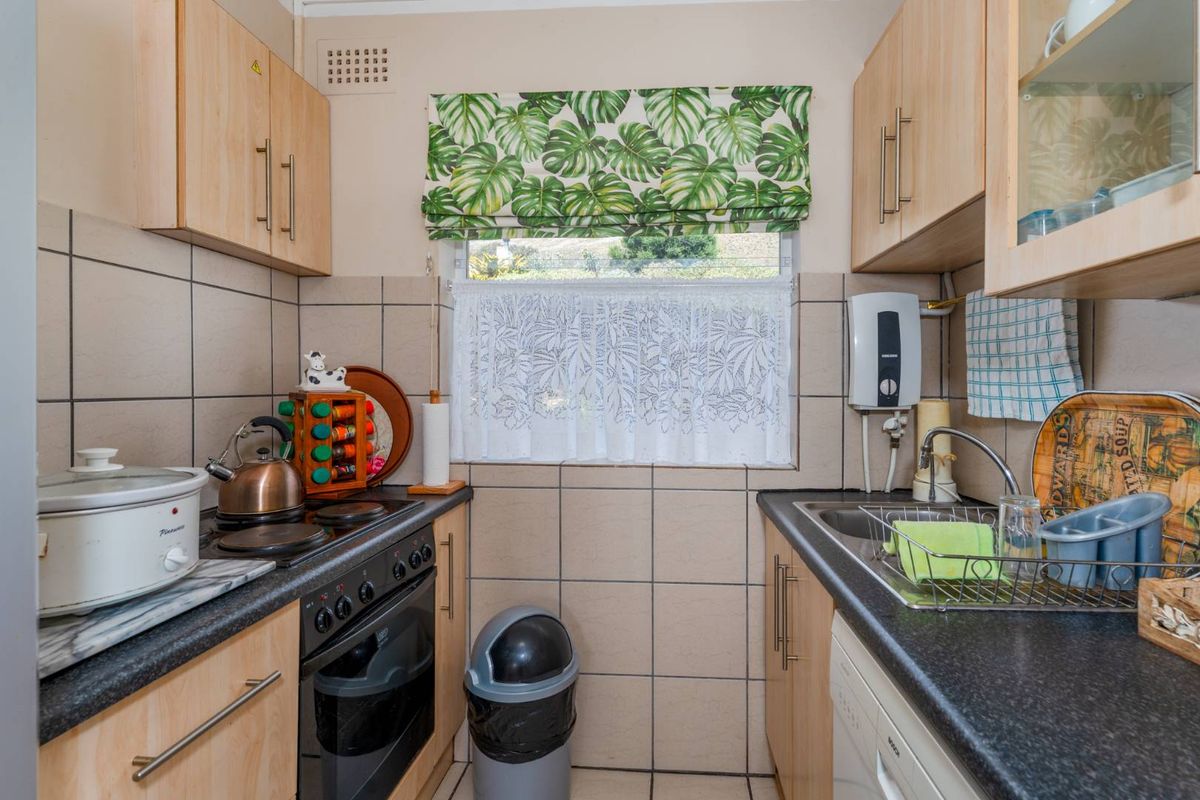 Compact kitchen featuring light wood cabinetry, dark laminate countertops, tiled splashbacks, and a built-in electric oven and hob.