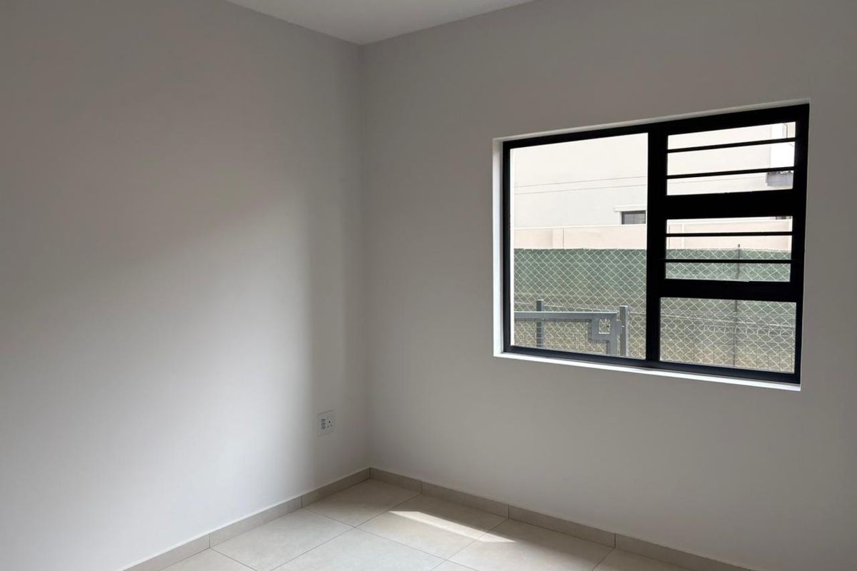 A clean, empty bedroom featuring neutral tiled flooring, fresh white walls, and a black aluminium window with integrated security bars.