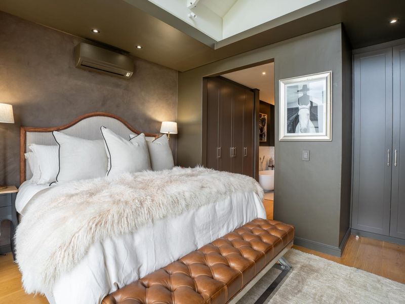 Elegant bedroom featuring vaulted ceilings, recessed lighting, hardwood flooring, and extensive built-in cabinetry with an adjoining en-suite bathroom.