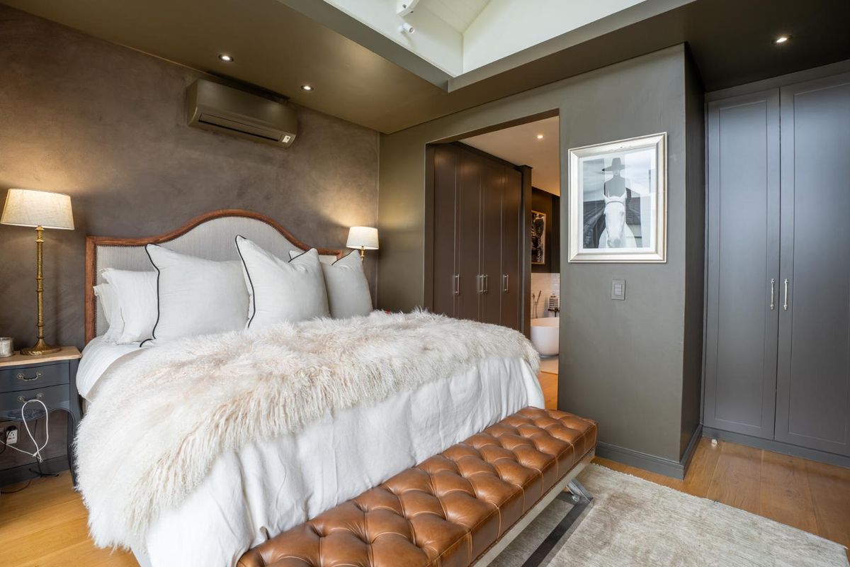 Elegant bedroom featuring vaulted ceilings, recessed lighting, hardwood flooring, and extensive built-in cabinetry with an adjoining en-suite bathroom.