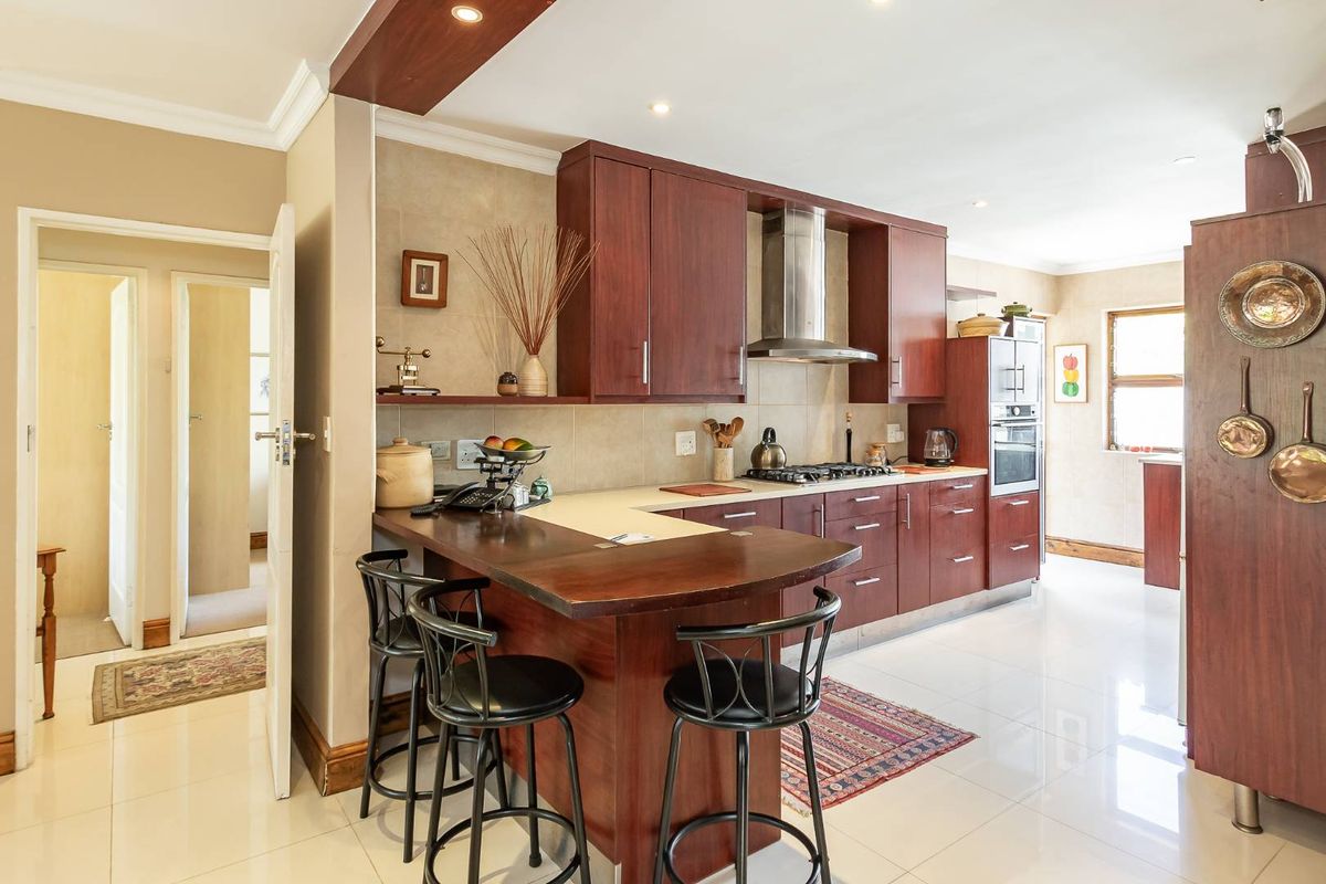 A functional kitchen featuring dark wood cabinetry, a breakfast bar, built-in oven, gas hob, and stainless steel extractor fan with tiled flooring.