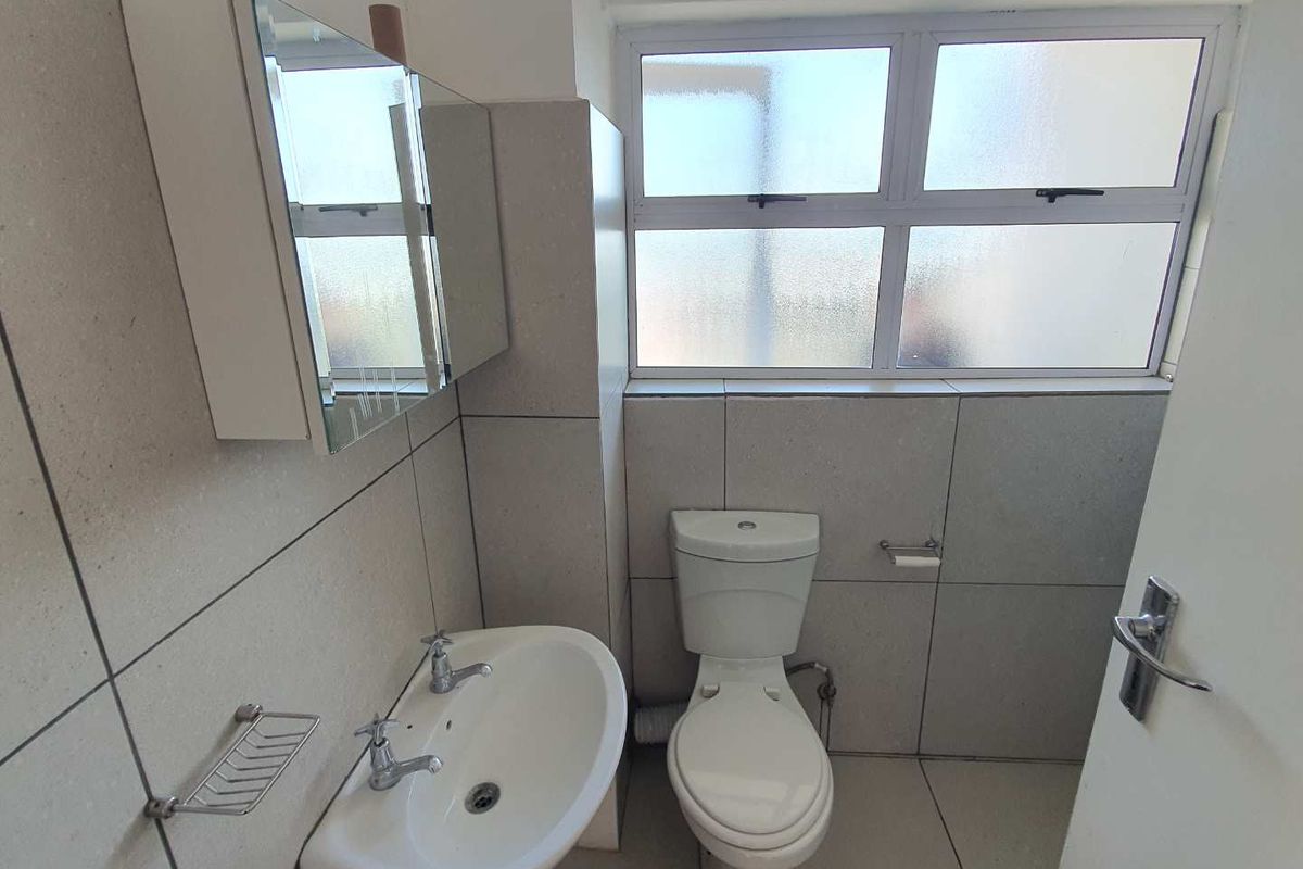 A functional bathroom featuring neutral wall tiles, a pedestal basin, a mirrored medicine cabinet, and a standard toilet.