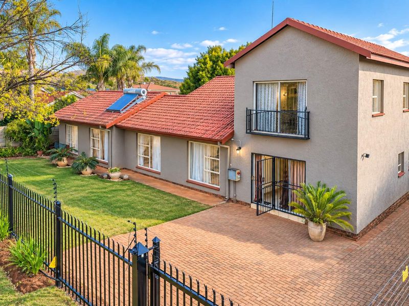 Rear view of the house featuring a paved patio area, landscaped garden, solar water heating system, and a balcony with security railings.