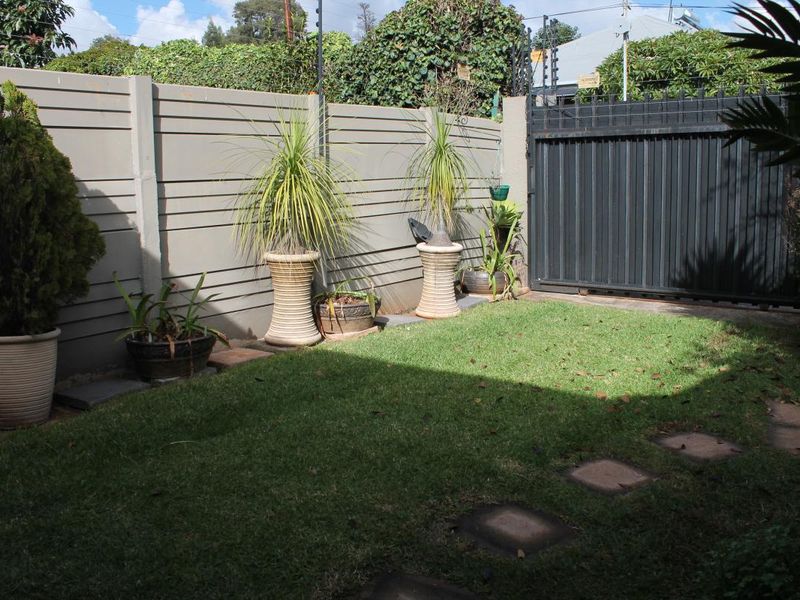 A private garden area featuring a well-maintained lawn, secure perimeter wall with electric fencing, and a sliding metal gate.