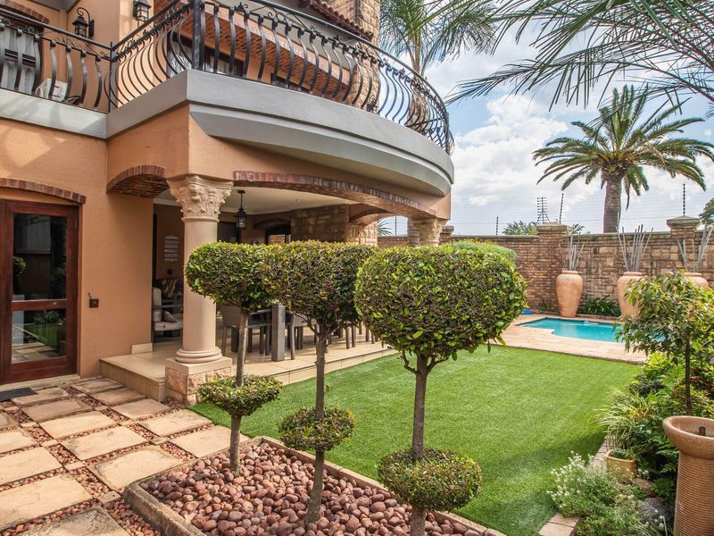 A well-maintained rear garden featuring a covered patio, swimming pool, manicured lawn, and a balcony with decorative wrought iron railings.