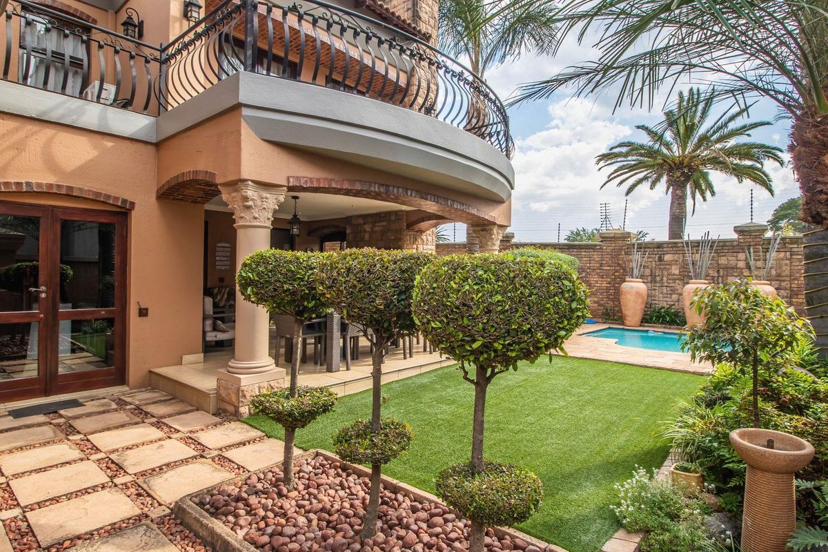A well-maintained rear garden featuring a covered patio, swimming pool, manicured lawn, and a balcony with decorative wrought iron railings.